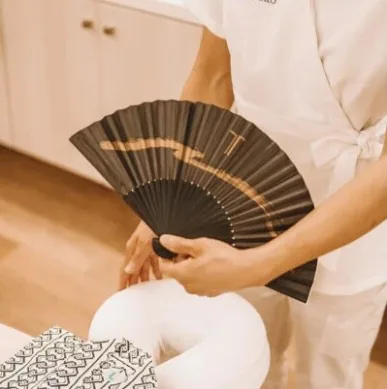 A therapist in white holding a black and gold folding fan